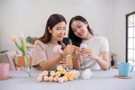 Middle-aged daughter happily arranges flowers with her mother at home Free time activities that are done together as a family.
