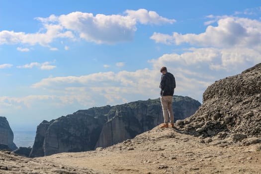 Experience the thrill of adventure as a tourist stands on the edge, gazing over the breathtaking cliffs of Meteora, Greece, on a radiant sunny day