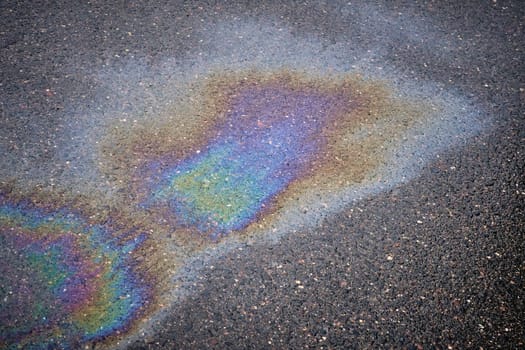 Close-up of an iridescent oil or gasoline spill on a wet asphalt, viewed from above. Bold multicolored spots on the asphalt. Concept of environmental problems.