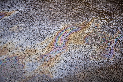Oil stains from leaks in the car engine. Oil after rain makes spots with rainbow reflections refractive sun spectrum