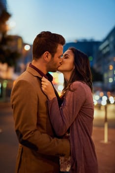 Couple, night and city with kiss on date, romance and bonding with love in relationship. Happiness, affection and people with commitment and trust, sweet moment and romantic together outdoor.