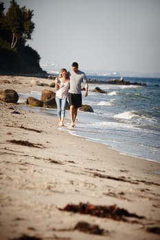 Couple, walking and hug on shore of beach, peace and travel to nature for holiday. People, embrace and calm on weekend trip or vacation, love and date for relationship or marriage and ocean waves.
