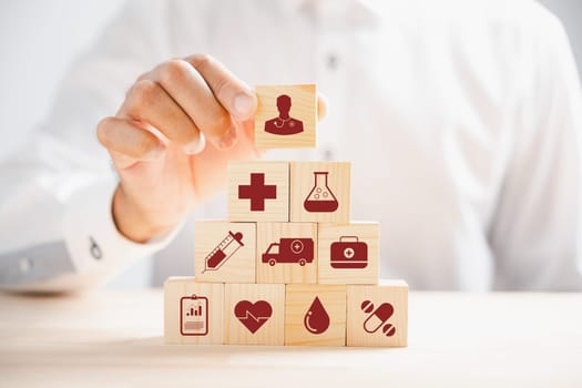 Hand holding wooden block featuring healthcare and medical icons symbolizes safety, health, and family well-being. Representing pharmacy, heart care, and happiness. health care concept