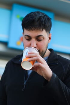 Witness the dynamic scene of a young man, his vitality evident, savoring a to-go coffee as he navigates through the bustling streets