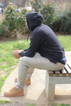 Enter the tranquil moment where a young man sits on a bench, enveloped in solitude and contemplation. With a serene demeanor, he gazes into the distance, lost in thought