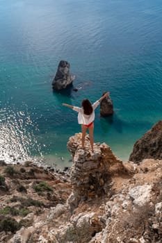 A woman is standing on a rock overlooking the ocean. She is enjoying the view