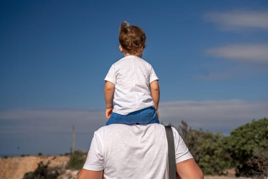 man is carrying a child on his back. The child is wearing a white shirt and blue shorts. The sky is clear and blue, and there are no clouds in the sky