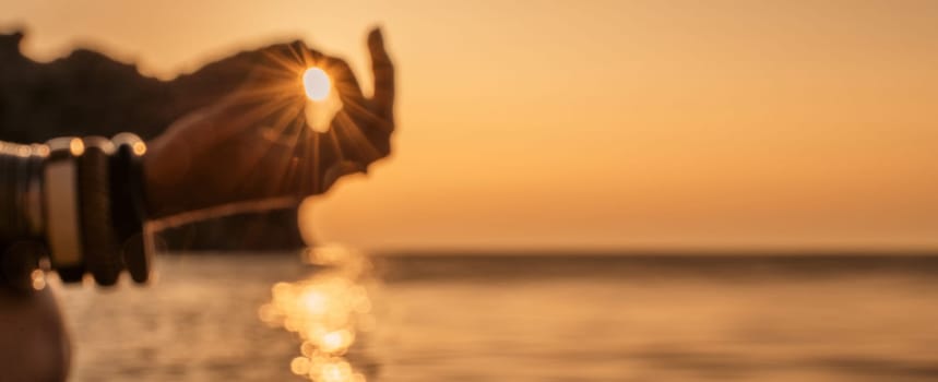 Banner. In blur closeup the hand of a young woman in bracelets. Practicing yoga on the beach with sunset. Keeps fingers connected, the sun shines through them. The concept of a healthy lifestyle, harmony