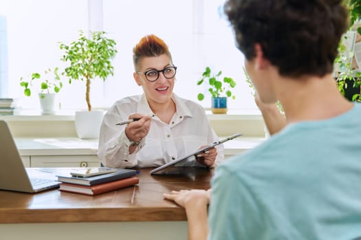 Middle-aged female professional psychologist mental therapist talking with young man in office. Psychotherapist advisor working with male patient. Psychology psychotherapy support treatment assistance