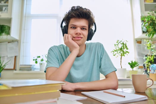 Webcam view of college student guy wearing headphones, talking looking at camera, sitting at desk in home. Young male studying online, video chat call conference, e-learning technology education