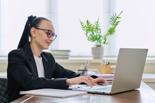 Business woman working in home office at desk with laptop computer. Smiling 30s female typing and looking at monitor. Remote business, technologies internet, teaching blogging work freelance concept