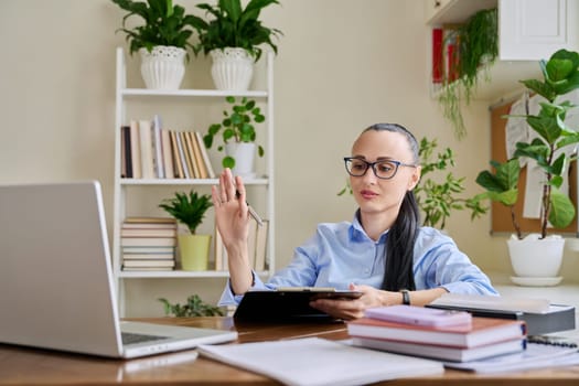 Confident successful business woman with clipboard sitting at workplace, looking at computer screen, talking to client employee patient. Remote business, technologies, internet, teaching, blog, work,