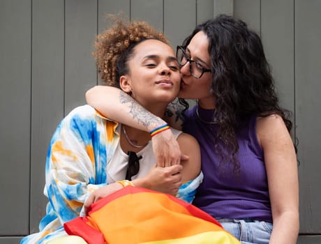 Women lesbian lovers are hugging and kissing. They wear a rainbow flag and bracelet to support LGBTQ community.