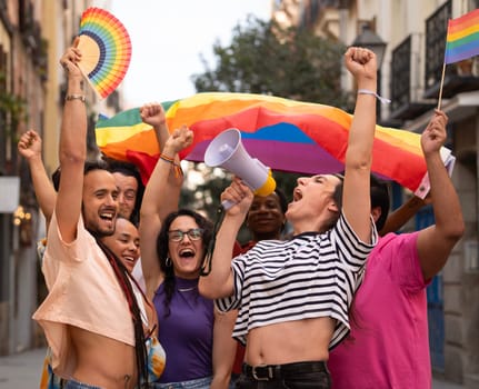 Group of LGBTQ people are holding rainbow flags and a megaphone during MADO party chueca pride gay day.