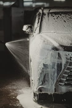 Man applying foam to black car in car wash. Vertical photo
