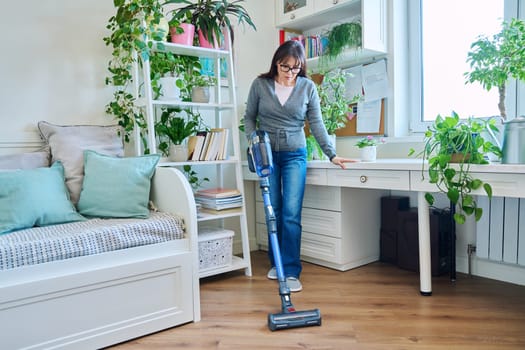 Middle aged female doing vacuuming at home. Cleanliness, routine house cleaning, home hygiene, housecleaning, housekeeping, housework concept