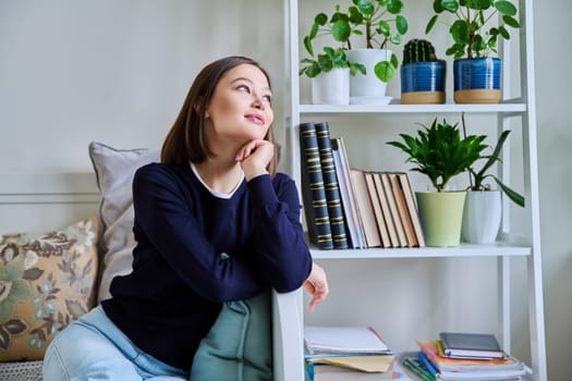 Portrait of young attractive smiling woman in home interior. Happy cheerful relaxed 20s female looking away, sitting on couch. Beauty, youth, happiness, health, lifestyle concept