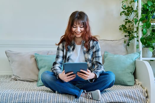 Young attractive trendy girl college student using digital tablet for studying communication leisure freelancing, sitting on couch at home. Technology, youth, education, lifestyle concept