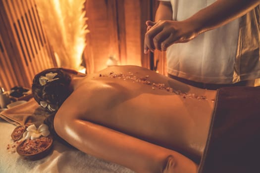 Woman customer having exfoliation treatment in luxury spa salon with warmth candle light ambient. Salt scrub beauty treatment in Health spa body scrub. Quiescent