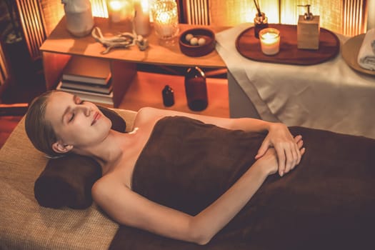 Caucasian woman customer enjoying relaxing anti-stress spa massage and pampering with beauty skin recreation leisure in warm candle lighting ambient salon spa at luxury resort or hotel. Quiescent