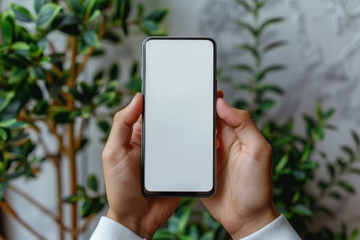 A man holds a cell phone with a white screen in front of a plant and takes a photo or video. Mockup