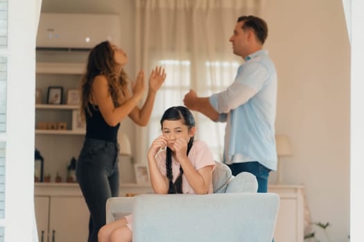 Annoyed and unhappy young girl sitting on sofa trapped in middle of tension by her parent argument in living room. Unhealthy domestic lifestyle and traumatic childhood develop to depression.Synchronos