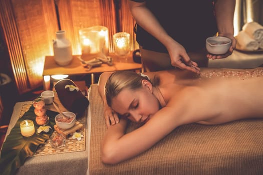 Woman customer having exfoliation treatment in luxury spa salon with warmth candle light ambient. Salt scrub beauty treatment in Health spa body scrub. Quiescent