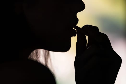 The silhouette of a woman engaging in a lip care ritual, her profile outlined against a warm sunset backdrop