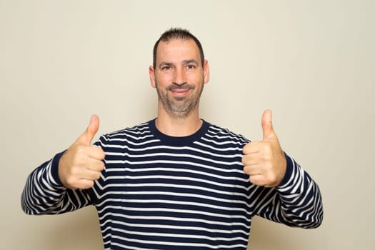 Bearded Hispanic man in his 40s wearing a striped sweater with thumbs up giving thumbs up to seaweed, isolated on beige studio background