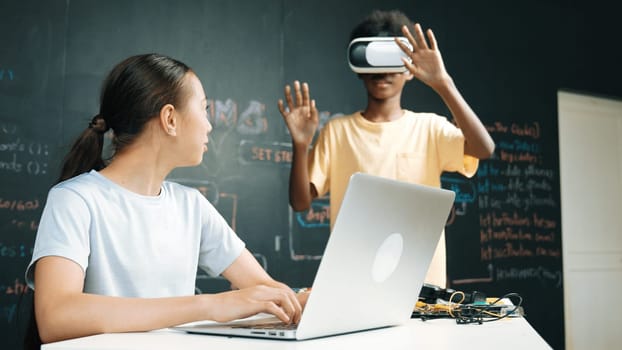 African boy wear headset to enter in metaverse while young beautiful academic student writing, coding, programing system on table with laptop or device placed. innovative education. Edification.