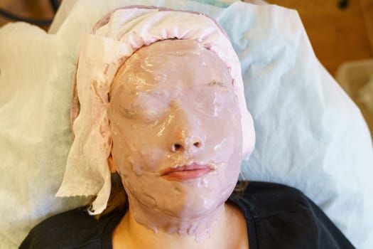 A woman having a facial mask applied during a skincare treatment at a beauty salon.