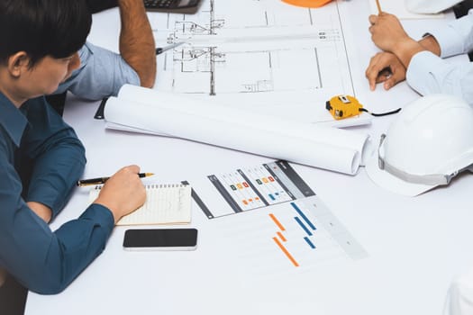 Diverse group of civil engineer and client working together on architectural project, reviewing construction plan and building blueprint at meeting table. Prudent