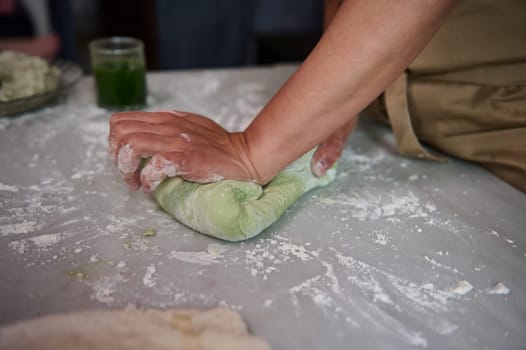 Close-up hands of housewife kneading dough on the floured kitchen table, preparing homemade dumplings for dinner, according to traditional recipe. Ingredients on the table. Homemade cuisine, culinary