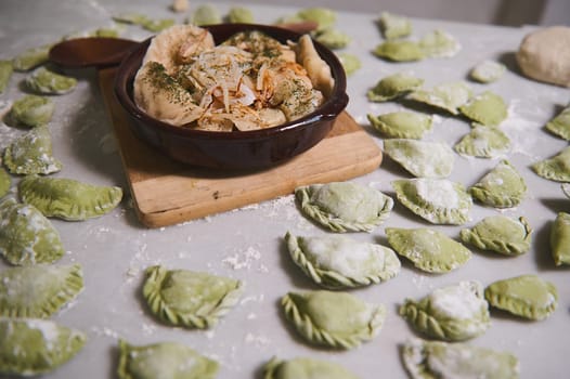 A clay plate with freshly prepared dumplings with mashed potatoes with steam, on the background of floured marble table with raw Ukrainian Varenyky. Culinary. Homemade cooking. Food background