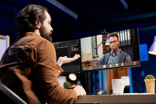 Developer doing software debugging helped by african american coworker in videocall, checking errors in lines of code. Man fixing coding mistakes assisted by colleague in internet videoconference