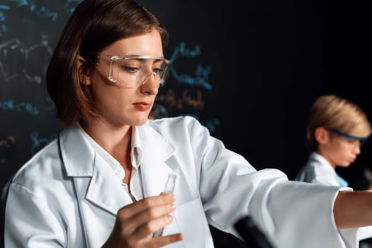 Teacher support schoolboy learning science of chemistry do experiment in laboratory wear lab coat and safety glasses in STEM class. Teacher manage test tube on the table with confidence. Erudition.