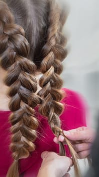 Hairdresser weaves a braid to a preteen blond girl