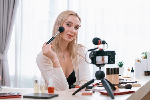 Young woman making beauty and cosmetic tutorial video content for social media. Beauty blogger smiles to camera while showing how to apply mascara to audience or followers. Blithe