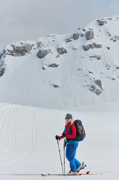 A determined skier scales a snow-capped peak in the Alps, carrying backcountry gear for an epic descent