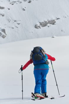 A determined skier scales a snow-capped peak in the Alps, carrying backcountry gear for an epic descent