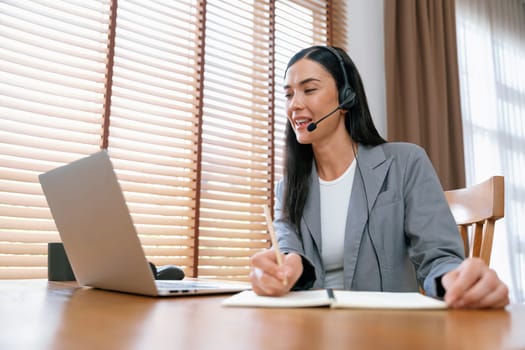 Female call center operator or customer service helpdesk staff working on workspace while talking on the headset to provide assistance for customer. Professional modern business service. Blithe