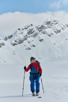 A determined skier scales a snow-capped peak in the Alps, carrying backcountry gear for an epic descent