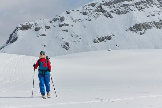 A determined skier scales a snow-capped peak in the Alps, carrying backcountry gear for an epic descent