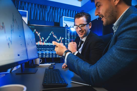 Two stock exchange traders comparing dynamic investment graph via phone and pc with high profit in currency rate. Showing financial benefit data on monitor screen in neon light at workplace. Sellable.