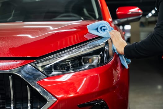 A man wipes the headlights of a red car with a microfiber cloth