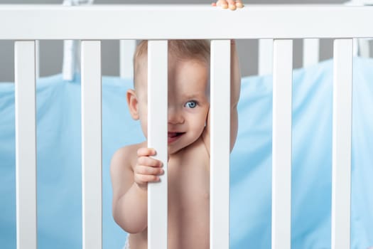 A baby peeks through the bars of a wooden crib.