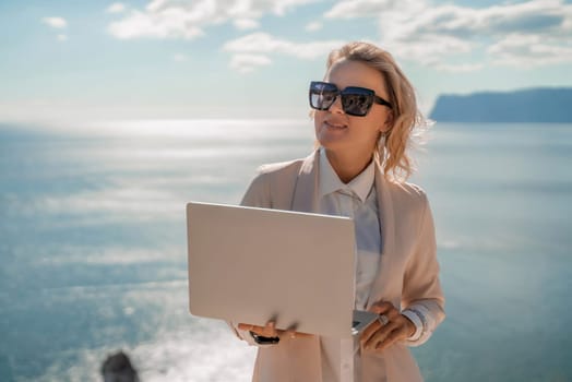 Freelance women sea. She is working on the computer. Good looking middle aged woman typing on a laptop keyboard outdoors with a beautiful sea view. The concept of remote work