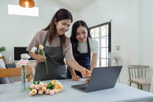 mother and daughter arrange flowers together as a hobby. mother and daughter spend free time doing flower arranging activities together and looking at laptop.