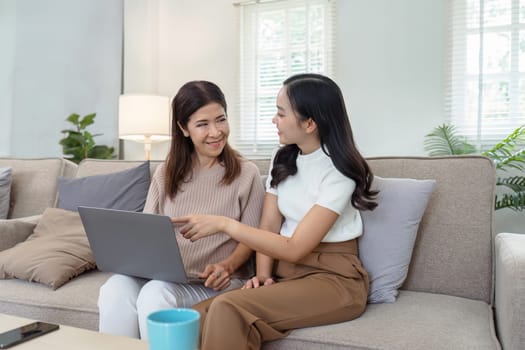 Mother and adult daughter sitting on the sofa together, mother and daughter using laptop to surf website together.