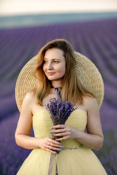 Woman poses in lavender field. Happy woman in yellow dress holds lavender bouquet. Aromatherapy concept, lavender oil, photo session in lavender.